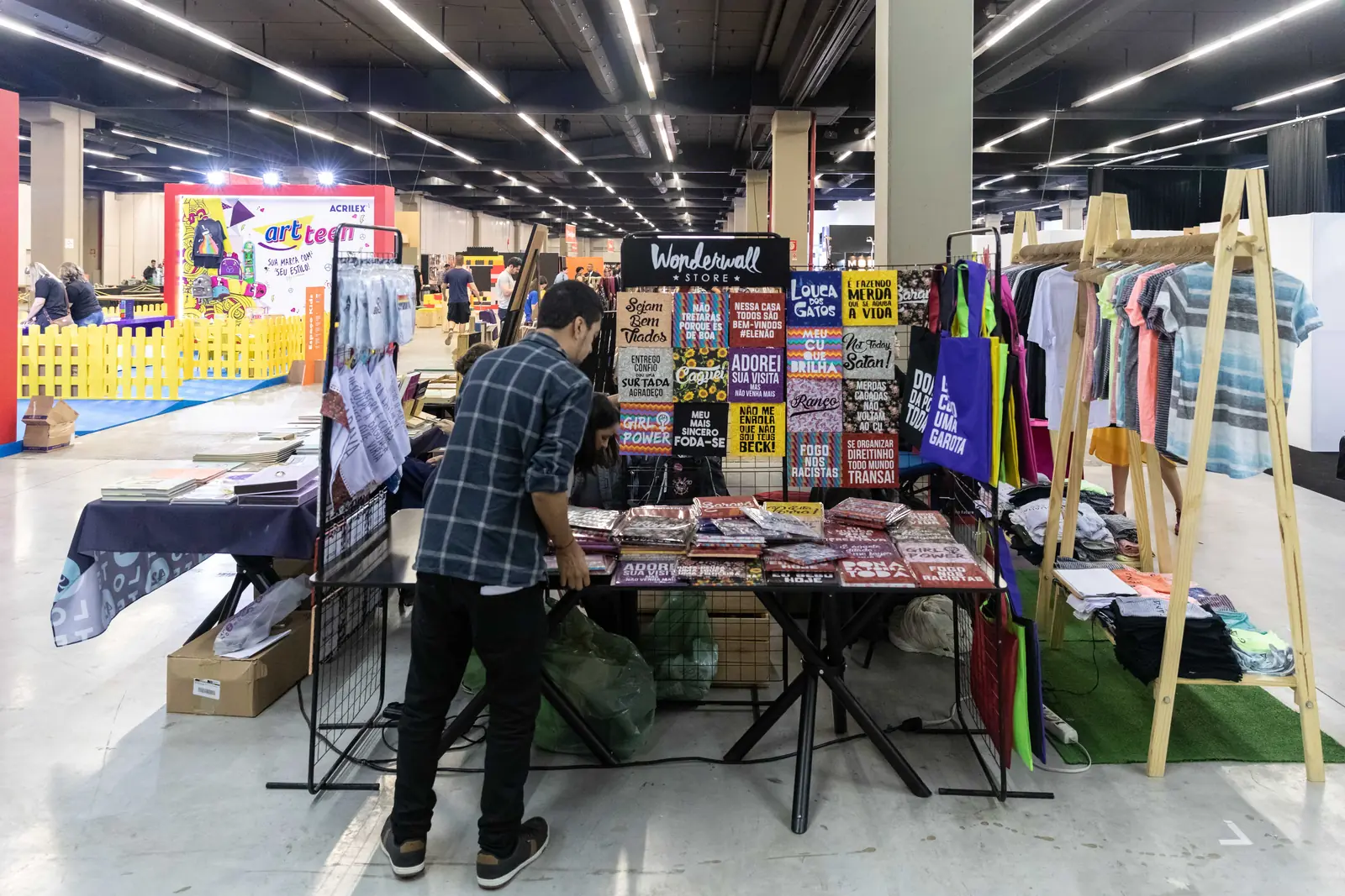 Expositor arrumando a banca de camisetas, pôsteres e livros no Pixel Show 2019