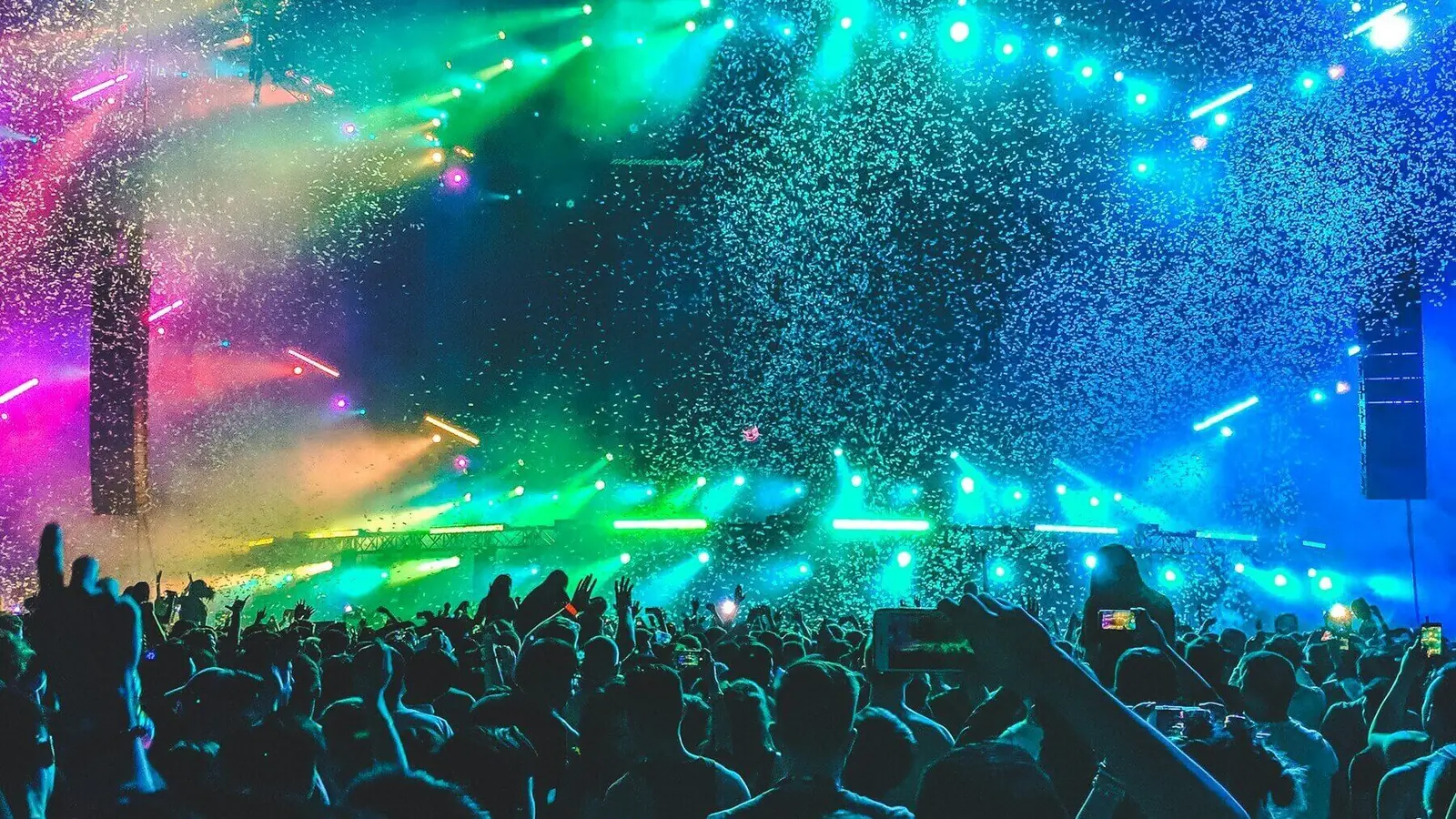 Show com luzes verdes e azuis, chuva de papel picado e o público com as mãos para cima