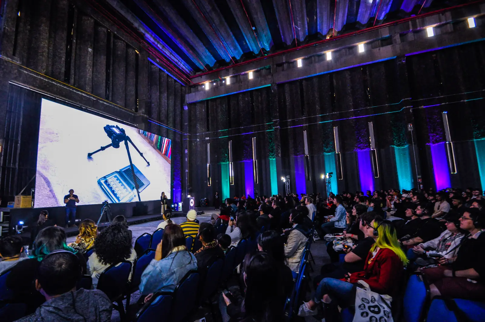 Plateia lotada na conferência do Pixel Show 2022, de frente para o palco com telão e luzes azuis e roxas