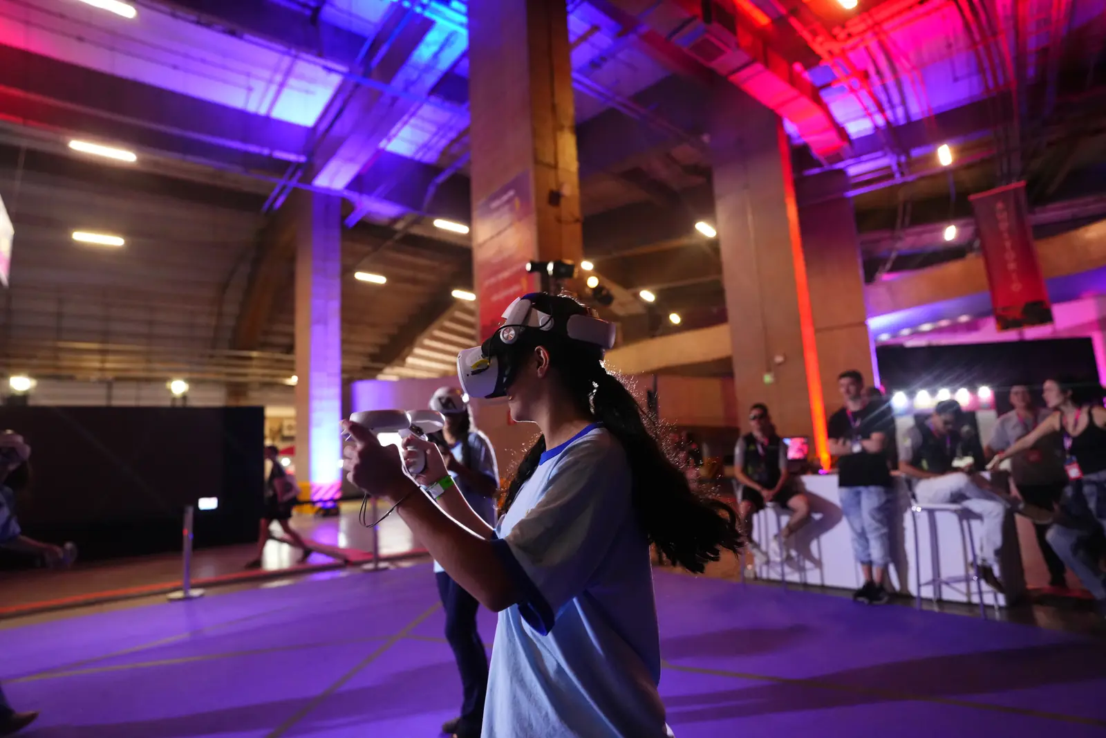 Pavilhão do Pixel Show com luzes roxas e vermelhas e uma pessoa usando óculos de realidade virtual