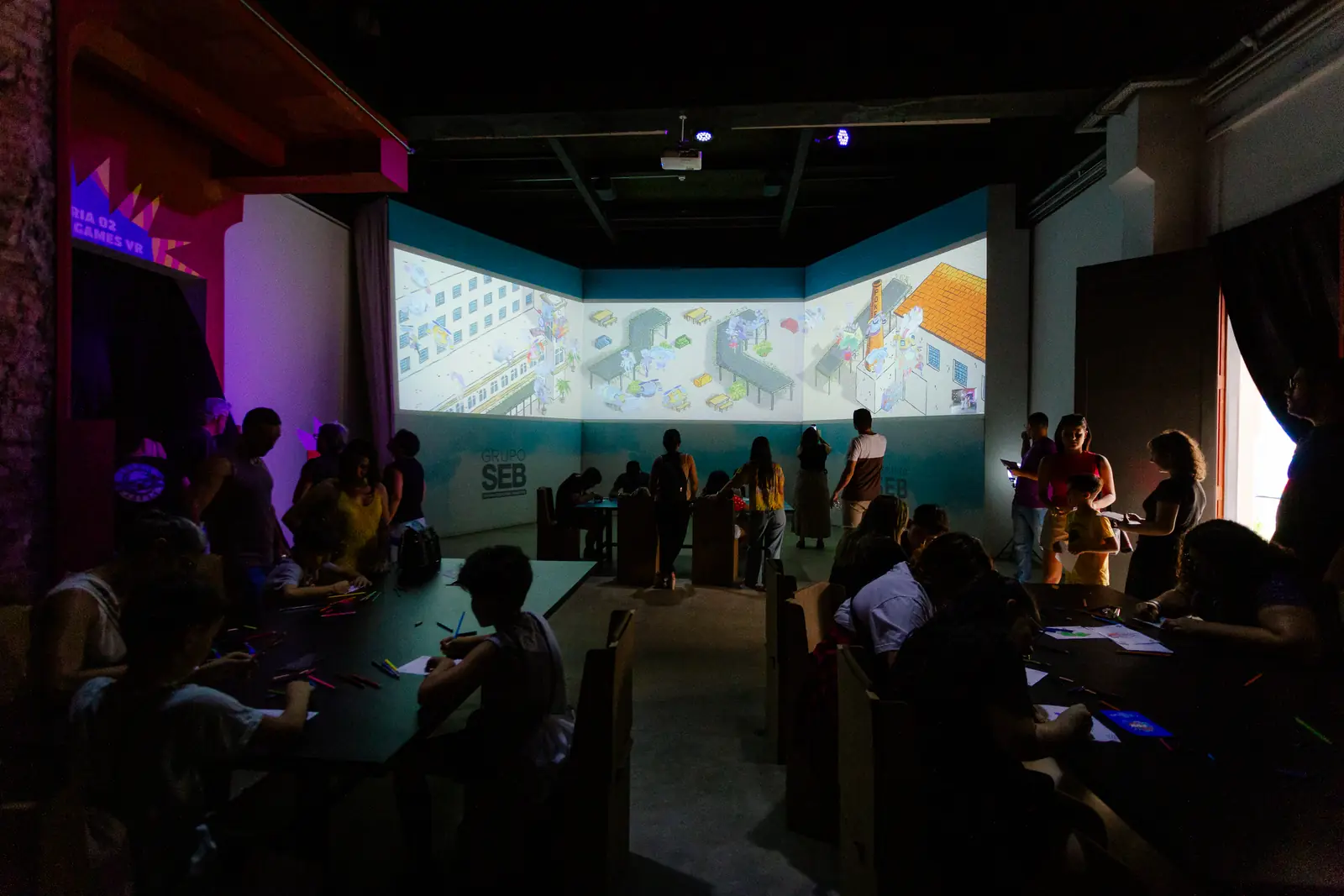 Sala imersiva do Zupi Space, com projeção colorida nas paredes e o público no escuro